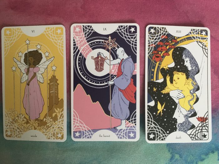 Photo of three cards: the six of wands, the hermit, death. The cards are colorful and have circles and stars in each of their corners.