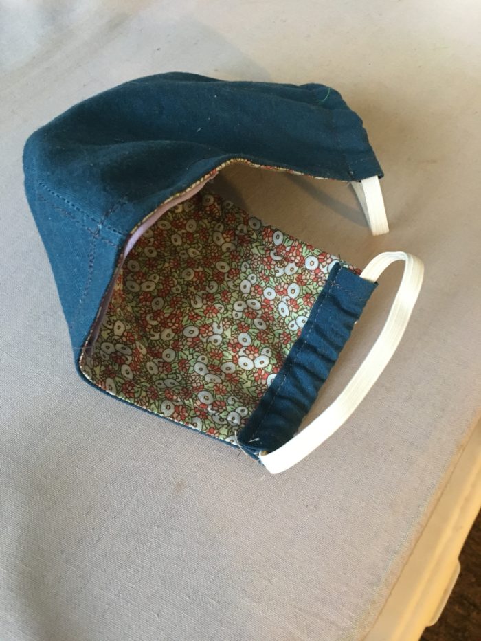 A face mask with elastic ear straps and a floral lining.